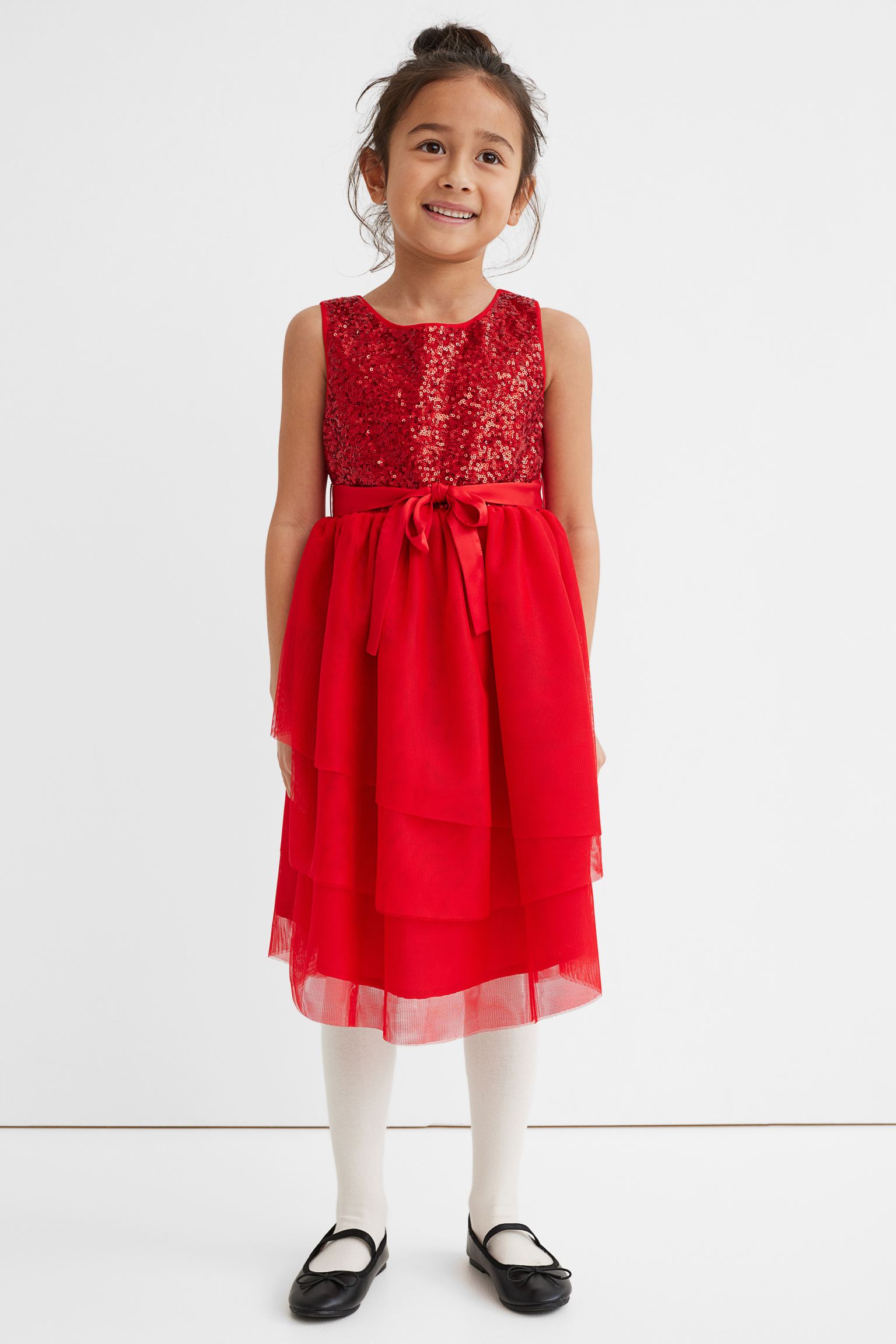 Vestido con cuerpo de lentejuelas. Modelo con cintura entallada, cinturón de anudar extraíble en satén y cierre de botones en la espalda. Falda en varias capas asimétricas de tul para dar volumen y vuelo.