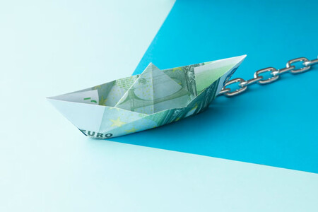 Barco de papel hecho con un billete de 100 euros que tiene una cadena unida a él