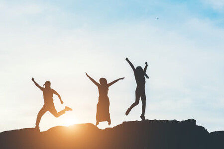 Siluetas de tres personas felices saltando con el sol a la espalda
