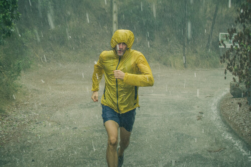 Homem de capa amarela correndo na chuva