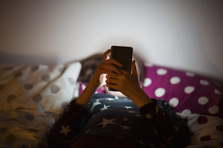 criança mexendo em celular deitado na cama