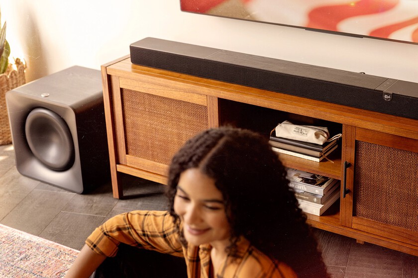 Klipsch Flexus Core 300 Bk And Sub 200 In Focus In Sunny Living Room With American Flag On Tv And Woman In Blurred Foreground 2000x1000