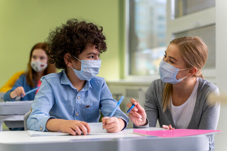 Female Teacher With Medical Mask Helping Students In Class